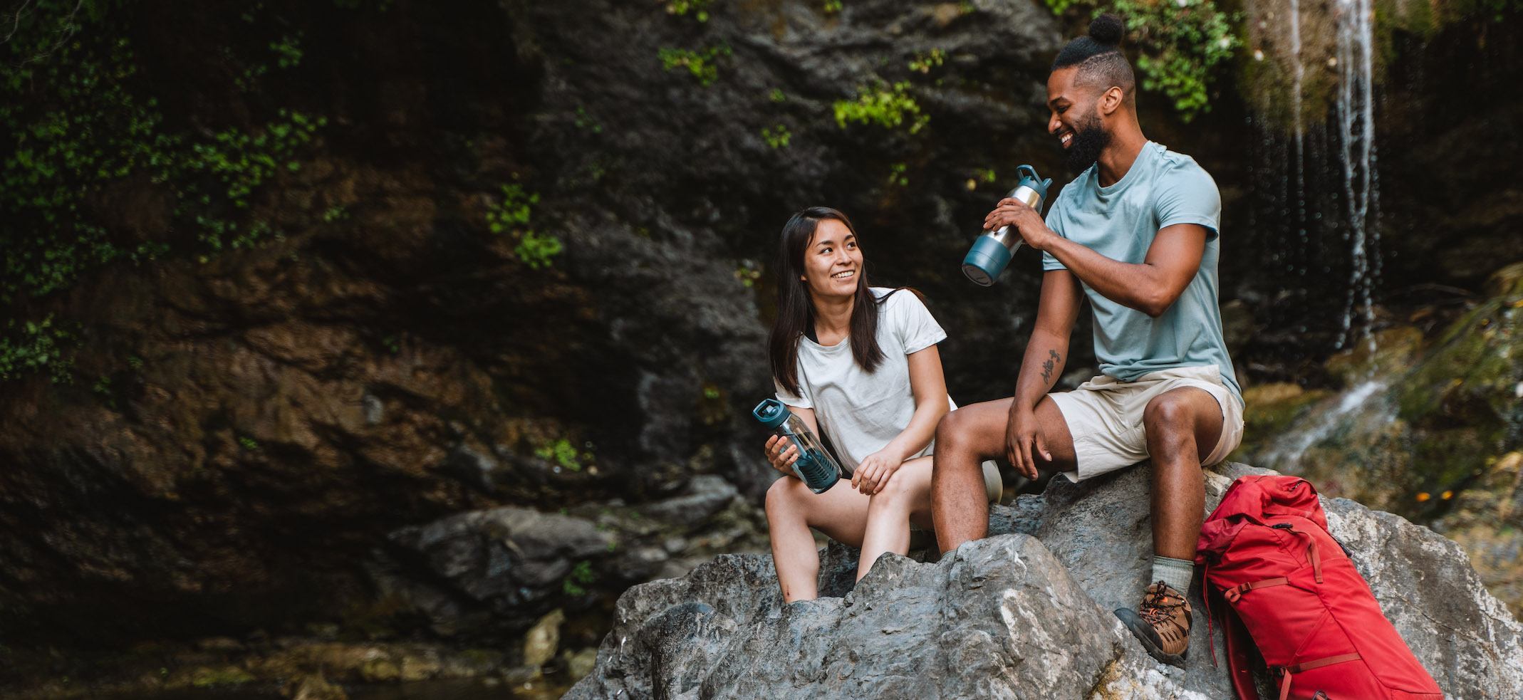 Man and Woman Drinking from RapidPure Water Bottles In Front of a Waterfall